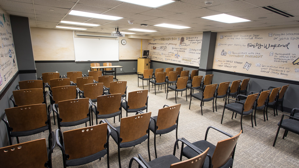 Six Rows of seven to eight chairs facing the front of the room, featuring a table and two chairs, whiteboard, projector, podium and computer.
